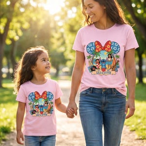 May include: Pink t-shirts featuring a colorful graphic of Lilo & Stitch, with a Mickey Mouse ear design and a red bow. The shirts are worn by a woman and a child, holding hands outdoors.