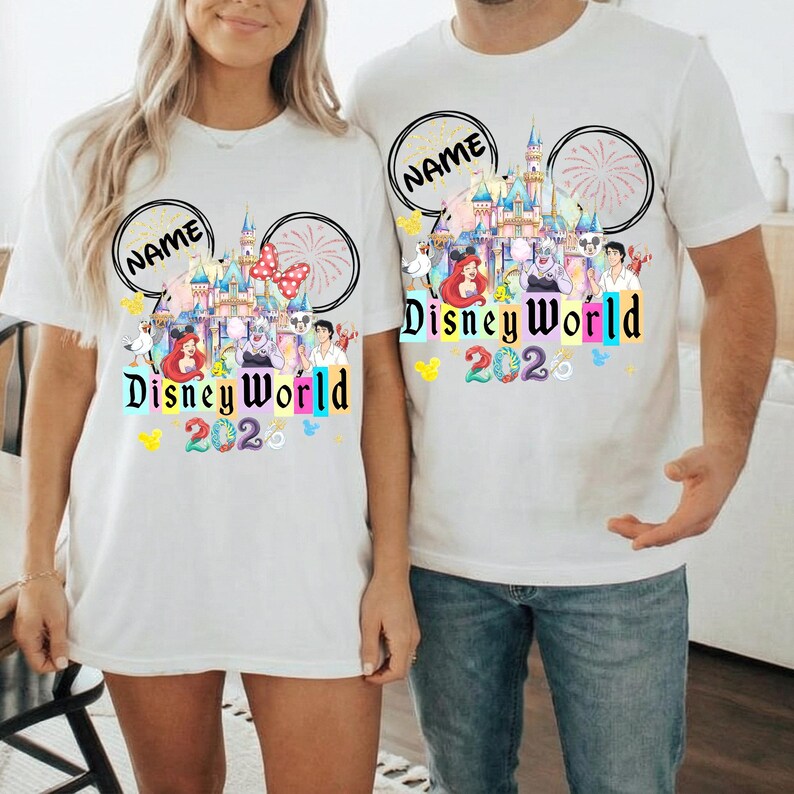 Puede incluir: Camisetas blancas con un dise&ntilde;o de Disney World 2020. El dise&ntilde;o incluye un castillo, fuegos artificiales y varios personajes de Disney. El texto "Disney World 2020" est&aacute; en letras coloridas. Las camisetas tienen un dise&ntilde;o de orejas de Mickey Mouse con la palabra "NAME" en un c&iacute;rculo.