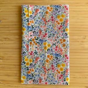 Könnte beinhalten: Ein rechteckiges Stoffstück mit einem dichten, farbenfrohen Blumenmuster auf weißem Hintergrund. Das Design besteht aus kleinen gelben, rosa, blauen und orangefarbenen Blüten, die mit grünen Blättern und Stängeln durchsetzt sind und einen lebendigen Druck bilden.