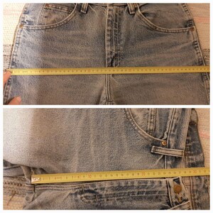May include: Light blue denim jeans with a straight leg cut. A yellow measuring tape is laid across the jeans, showing a measurement of approximately 48 inches across the waist. The jeans have classic five-pocket styling.