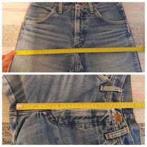 May include: Light blue denim jeans with a high waist, featuring a classic five-pocket design. The jeans are measured with a yellow tape measure, showing the waist and inseam dimensions. The fabric has a faded, worn look.