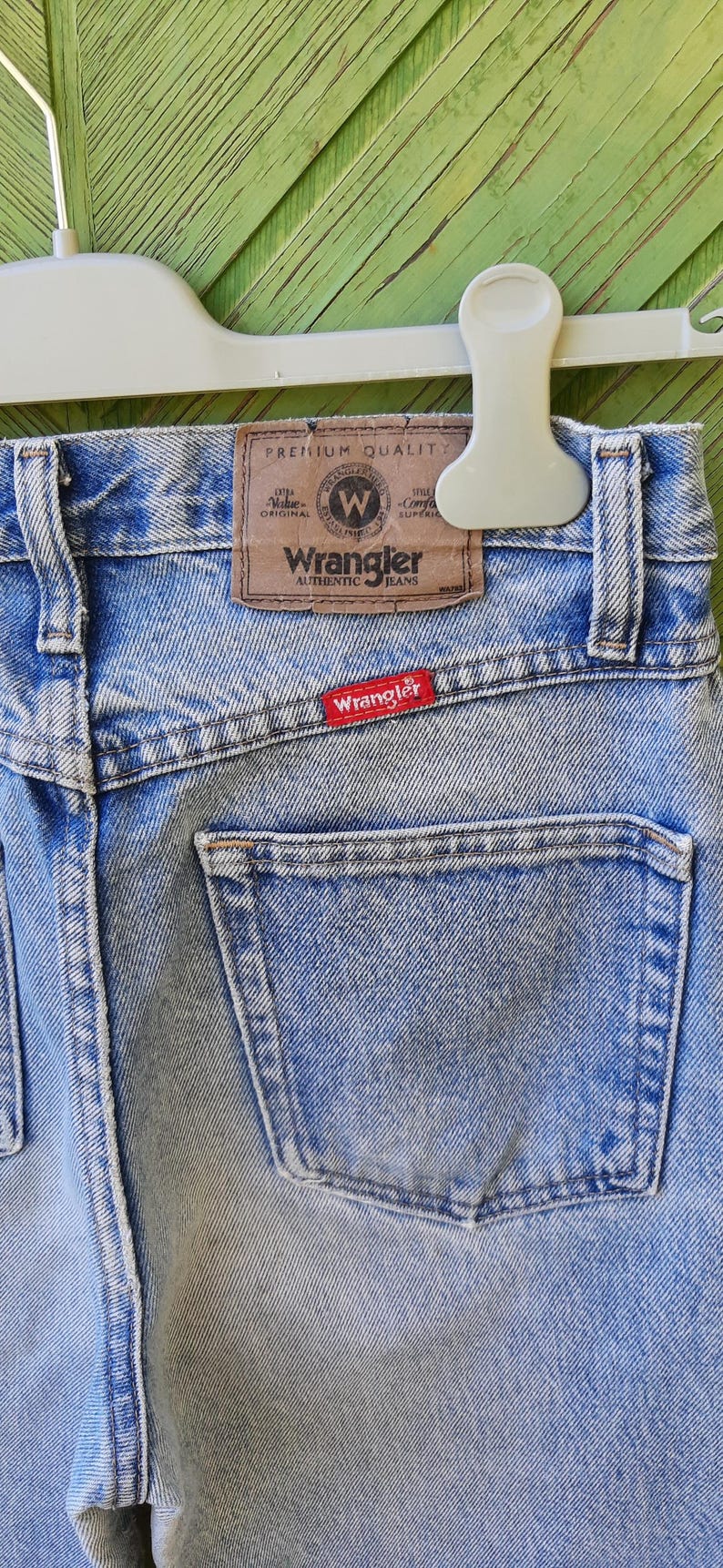 May include: Light blue Wrangler jeans with a classic design. The back of the jeans features a pocket and a brown leather patch with the Wrangler logo. A red Wrangler tag is sewn on the back pocket.