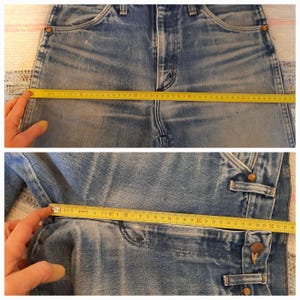 May include: Blue denim jeans featuring a high-waisted design with copper-toned rivets and a button fly. A yellow measuring tape is placed across the waist and hip areas, showing widths of approximately 18 inches and 12 inches respectively.