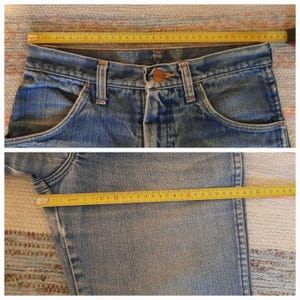 May include: Close-up of blue denim jeans with a button closure and pockets. A yellow measuring tape shows the waist is approximately 15 inches wide. The jeans are on a patterned surface.