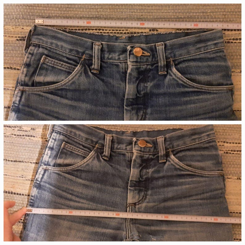 May include: Two pairs of blue denim jeans with a copper button and a single pocket on each side. The jeans are laid flat on a woven surface and measured with a tape measure.