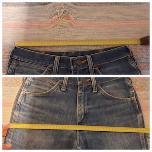 Pode incluir: Close-up de jeans azuis com fecho de bot&atilde;o e bolsos. Uma fita m&eacute;trica amarela mostra que a cintura tem aproximadamente 86 cm de largura. Os jeans est&atilde;o colocados sobre uma superf&iacute;cie texturizada.