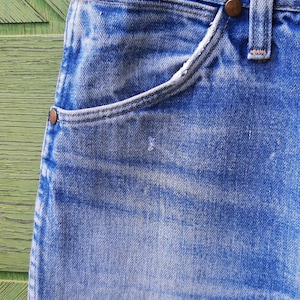 May include: A pair of light blue denim jeans featuring a classic five-pocket design with a high-waisted cut, copper-toned metal rivets at the pocket corners, a sturdy waistband with belt loops, and a visible light wash finish on the fabric.