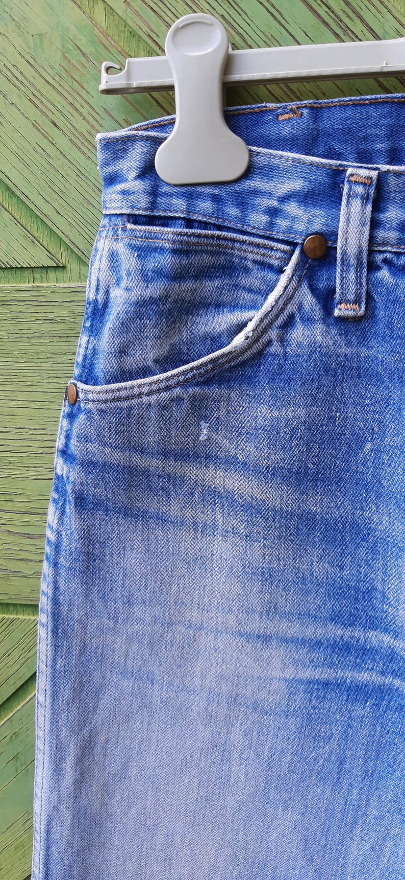 May include: A pair of light blue denim jeans featuring a classic five-pocket design with a high-waisted cut, copper-toned metal rivets at the pocket corners, a sturdy waistband with belt loops, and a visible light wash finish on the fabric.