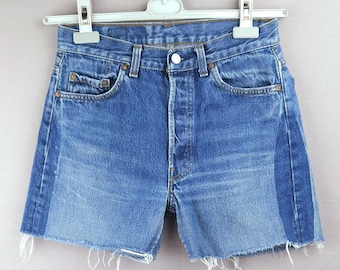 May include: Blue denim shorts featuring a high-waisted design with a button fly closure, five pockets, and raw, frayed hems. The garment displays a two-tone color effect with lighter blue center panels and darker blue side panels.