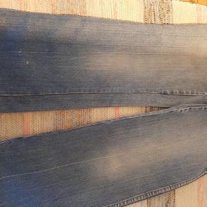 May include: Faded blue denim jeans with a classic five-pocket design. The jeans have a relaxed fit and a light wash, showing subtle wear patterns. The fabric appears soft and well-worn, suggesting comfort and durability.