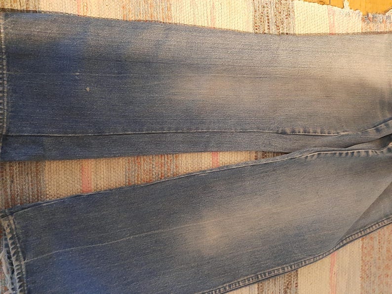 May include: Faded blue denim jeans with a classic five-pocket design. The jeans have a relaxed fit and a light wash, showing subtle wear patterns. The fabric appears soft and well-worn, suggesting comfort and durability.