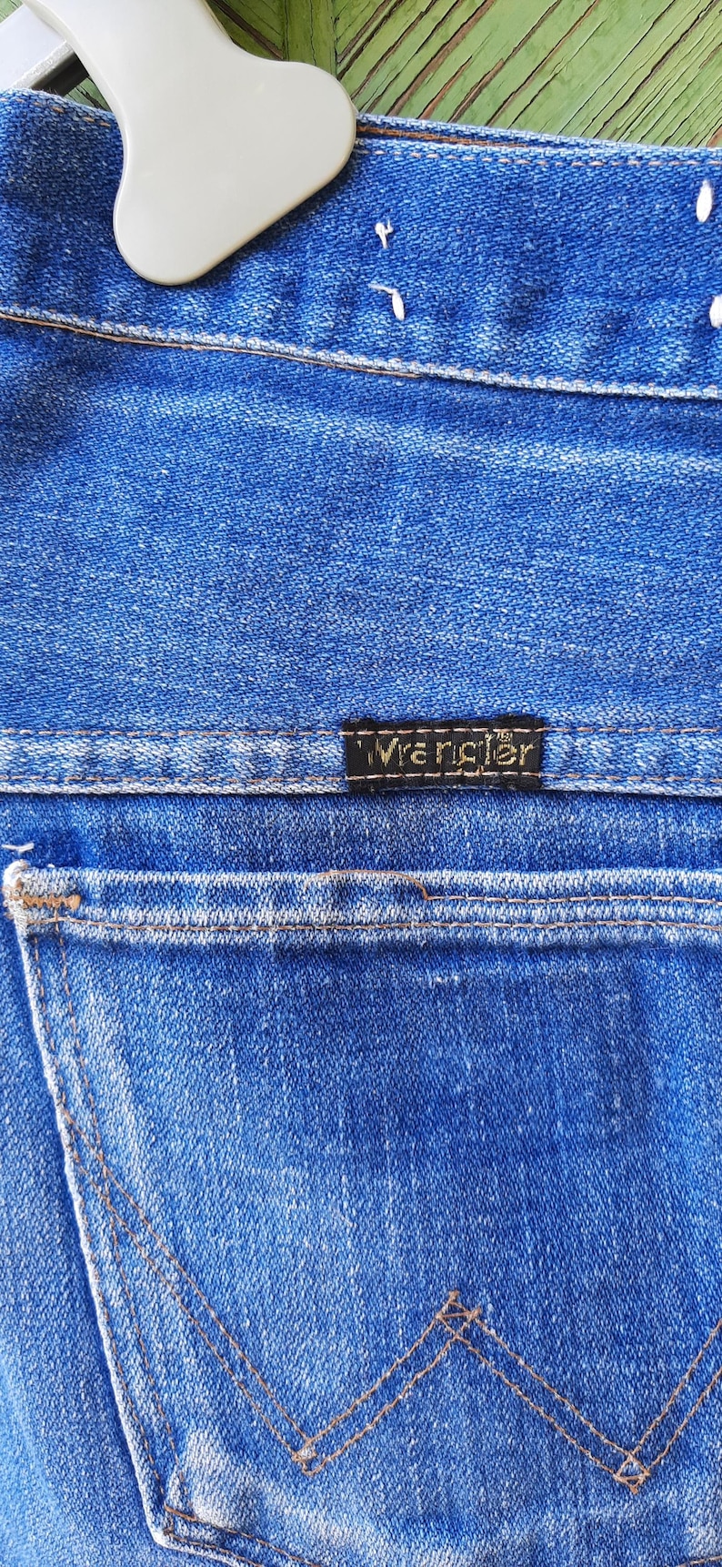 May include: Close-up of blue denim jeans with the brand name "Wrangler" on a black label. The jeans have a classic five-pocket design with visible stitching and a back pocket.