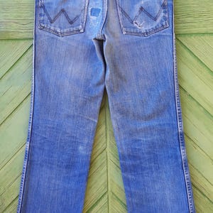 May include: A pair of blue denim jeans with a wide leg opening. The jeans have a faded look and have a small tear on the back right pocket.