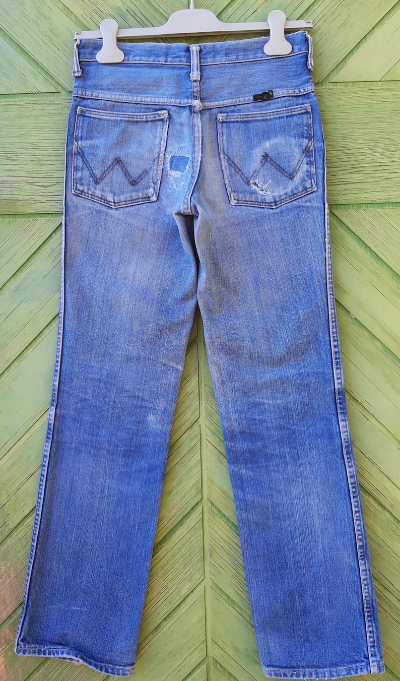 May include: A pair of blue denim jeans with a wide leg opening. The jeans have a faded look and have a small tear on the back right pocket.