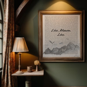 May include: A framed print with a black and white illustration of mountains and a bird flying over them. The print has a white background and the text "Live.  Maven.  Live." is printed in black on the bottom of the print. The print is hanging on a dark green wall.