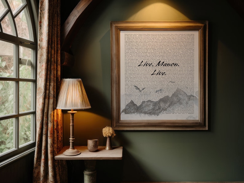 May include: A framed print with a black and white illustration of mountains and a bird flying over them. The print has a white background and the text "Live.  Maven.  Live." is printed in black on the bottom of the print. The print is hanging on a dark green wall.