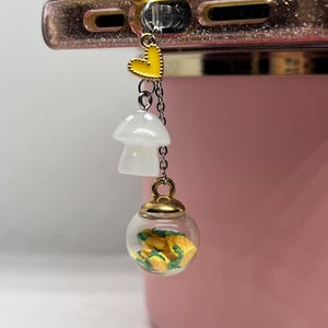 May include: A phone charm with a clear glass orb filled with yellow and green miniature pineapples, a white mushroom charm, and a yellow heart charm.
