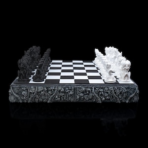 Puede incluir: Un juego de ajedrez blanco y negro con un tablero esculpido y detallado con temática de calavera. Las piezas de ajedrez están dispuestas en el tablero en posición inicial.