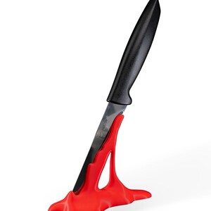 May include: A red plastic knife holder shaped like a wave with a black handled knife inserted into it.