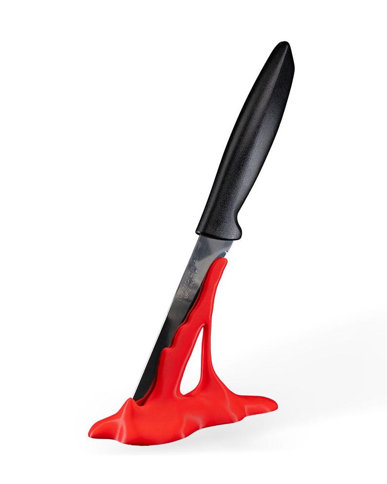 May include: A red plastic knife holder shaped like a wave with a black handled knife inserted into it.