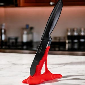 May include: A red plastic knife holder with a black kitchen knife inserted. The knife has the text "Tramontina Made in Brazil" on the blade.