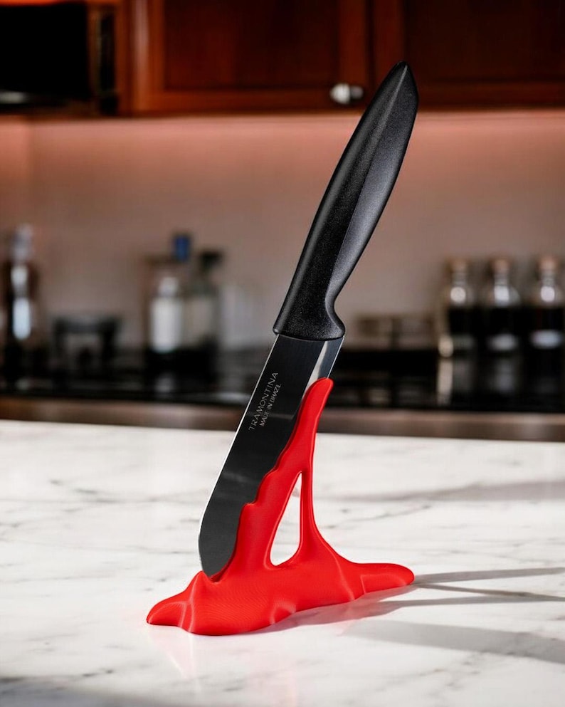 May include: A red plastic knife holder with a black kitchen knife inserted. The knife has the text "Tramontina Made in Brazil" on the blade.