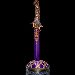 May include: A decorative sword with a purple blade and a gold and brown handle with intricate details. The sword is on a round base with a purple and gold design.