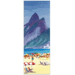 May include: A cross-stitch bookmark featuring a beach scene with mountains in the background. The scene includes a beach with people, umbrellas, and lounge chairs. The mountains are purple and green, and the sky is blue.
