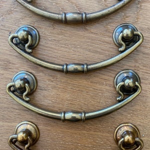 May include: Four antique-style,  bronze-colored drawer pulls with a curved design. Each pull has a decorative knob at the top and a rounded center.