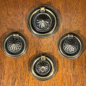 May include: Four antique gold-toned cabinet knobs with a decorative floral design and a ring pull.