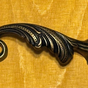 May include: A decorative, ornate, black and gold metal cabinet pull with a floral design.