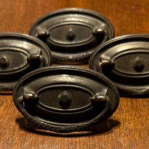 May include: Four antique oval-shaped cabinet knobs with a decorative design and a black finish.