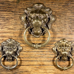 May include: Three brass lion head door knobs with ring pulls. The lion heads are detailed with a textured finish and have a realistic appearance.