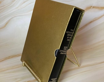 May include: A gold-colored book with a black leather spine. The book is titled "The Alternative Service Book 1980" with "With The Liturgical Psalter" printed below. The book is on a gold-colored stand.