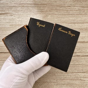 Può includere: Un set di due piccoli libri neri con copertine testurizzate e scritte in oro. Un libro è intitolato Hymnal e l'altro Common Prayer. I libri sono custoditi all'interno di un cofanetto protettivo nero abbinato con segni di usura sui bordi.