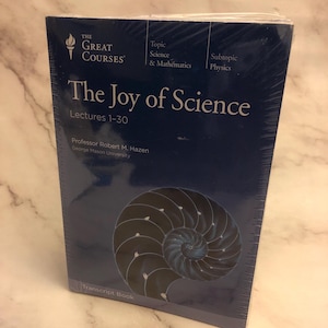 May include: A blue book titled "The Joy of Science" by Professor Robert M. Hazen. The book is part of The Great Courses series and covers lectures 1-30 on science and mathematics, with a subtopic of physics. The cover features a nautilus shell.