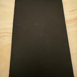 Könnte beinhalten: Ein rechteckiges, schwarzes, strukturiertes Materialstück. Das Material hat eine leicht raue Oberfläche und scheint einfarbig zu sein. Die Kanten sind sauber geschnitten, und die Gesamtform ist ein einfaches Rechteck.