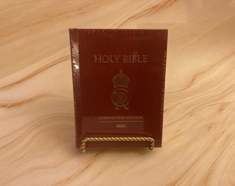 May include: A burgundy hardcover Holy Bible with gold lettering. The title "HOLY BIBLE" is printed on the front cover. The book also features a gold royal crest and the text "CORONATION EDITION 2023".
