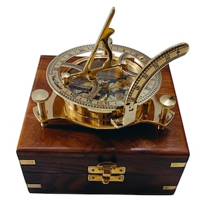 May include: A brass sundial with a compass and a wooden box. The sundial has a gold finish and is decorated with Roman numerals. The compass is also gold and has a clear glass face. The wooden box is dark brown and has a hinged lid.