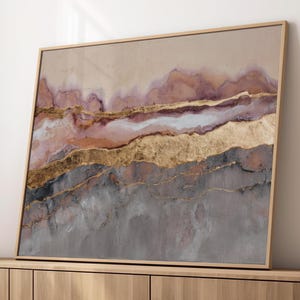 Peut inclure: Impression d'art abstrait dans un cadre en bois. L'œuvre présente des couches de couleurs, dont l'or, le gris, le rose et le beige, créant un design texturé semblable à un paysage. L'art encadré est exposé sur un meuble en bois.