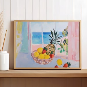 Könnte beinhalten: Ein gerahmter Kunstdruck zeigt ein Stillleben mit einer Ananas, Zitronen und Erdbeeren in einem geflochtenen Korb. Das Gemälde zeigt einen Blick auf das Meer durch ein Fenster. Der Rahmen ist goldfarben und das Kunstwerk steht auf einem Holztisch.