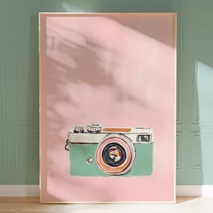 Könnte beinhalten: Ein gerahmter Druck einer Vintage-Kamera auf rosa Hintergrund. Die Kamera ist grün und weiß mit einem braunen Objektiv. Der Druck ist perfekt für eine minimalistische Einrichtung.
