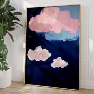 Könnte beinhalten: Abstrakter Kunstdruck mit dunkelblauem Hintergrund und rosa und weißen Wolkenformen. Das Kunstwerk ist in einem goldfarbenen Rahmen gerahmt und lehnt an einer weißen Wand. Eine Topfpflanze ist zu sehen.