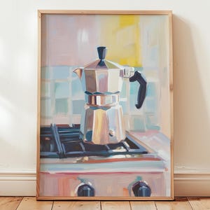 Könnte beinhalten: Gerahmtes Ölgemälde einer silbernen Espressokanne auf einem Gasherd. Das Kunstwerk ist in einer Küche mit Pastelltönen und einem hellen Holzrahmen dargestellt. Das Bild vermittelt eine warme, einladende Küchenatmosphäre.