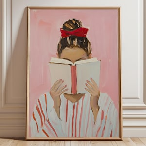 Könnte beinhalten: Ein Kunstdruck einer Person, die ein Buch liest, mit einer roten Schleife im Haar. Die Person trägt ein weißes Hemd mit roten Streifen. Der Hintergrund ist einfarbig rosa, und der Druck ist in einem goldenen Rahmen.
