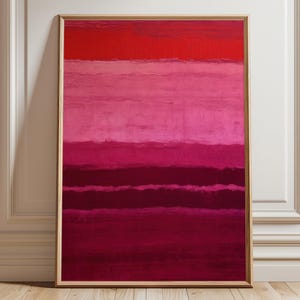 Puede incluir: Impresión artística abstracta enmarcada. La obra presenta bandas horizontales de colores rojos y rosas, creando un efecto degradado. La pintura se exhibe contra una pared blanca y un suelo de madera.