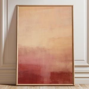 Könnte beinhalten: Abstrakter Kunstdruck in einem Holzrahmen. Das Kunstwerk zeigt einen Farbverlauf, der von hellem Pfirsich oben nach tiefem Rot unten übergeht. Das Gemälde lehnt an einer weißen Wand.