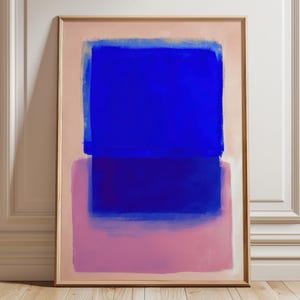 Könnte beinhalten: Abstrakter Kunstdruck mit Holzrahmen, der blaue und rosa rechteckige Formen auf hellrosa Hintergrund zeigt. Das Kunstwerk wird vor einer weißen Wand und einem Holzboden präsentiert. Die kräftigen Farben des Gemäldes erzeugen einen auffälligen visuellen Effekt.