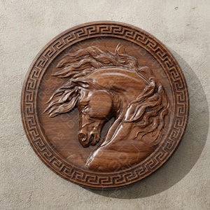 Pode incluir: Uma escultura de madeira de uma cabeça de cavalo em uma moldura circular com uma borda de chave grega. A escultura é de madeira marrom escura e a moldura é de madeira marrom clara.
