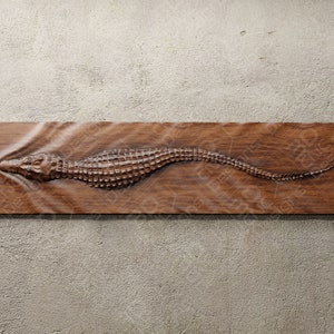 Puede incluir: Una placa de pared de madera con un diseño de cocodrilo tallado. El cocodrilo está representado nadando en el agua, con ondas talladas en la madera. La placa es de color marrón claro y tiene una veta de madera natural.